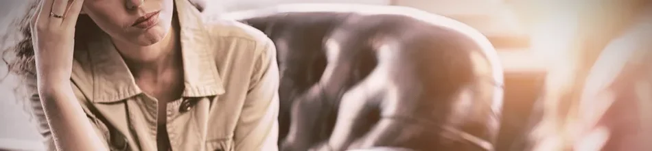 A patient in a therapists office sitting on a leather chair holding her forehead