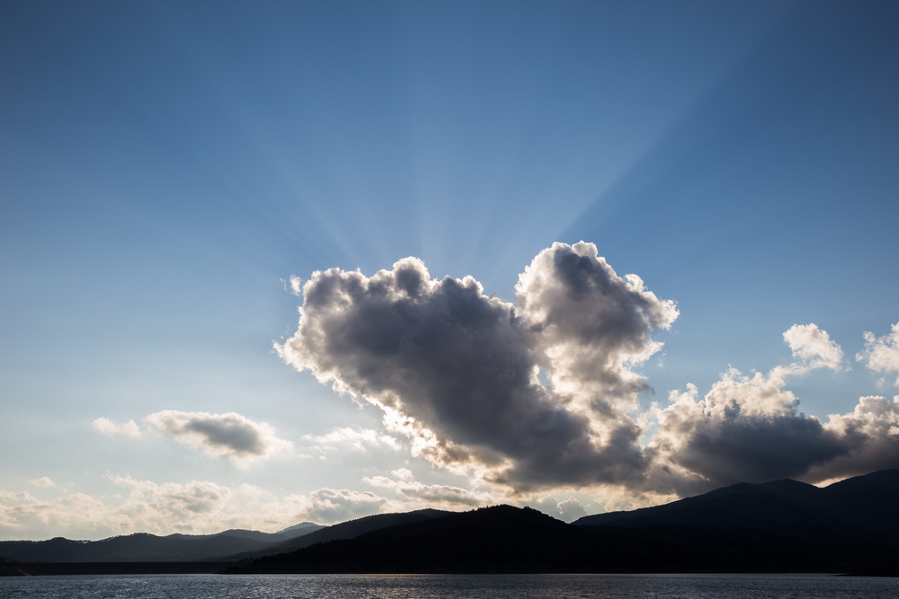 Sunrays coming out behind a cloud, above a lake and some mountains